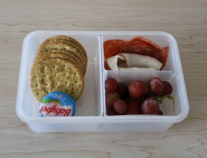 bento box with crackers, cheese, deli meat, and red grapes
