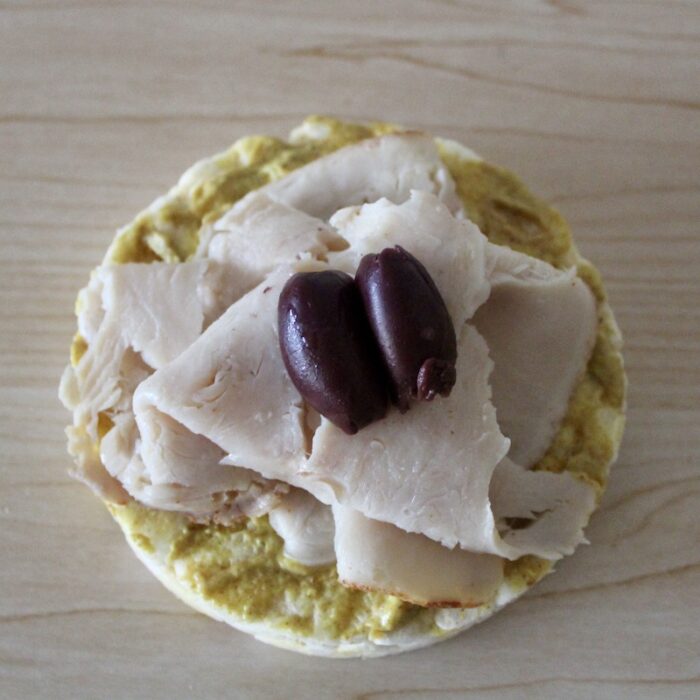 rice cake with mustard, deli turkey meat, and olives