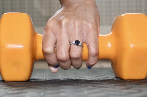 holding dumbbell with engagement ring on finger