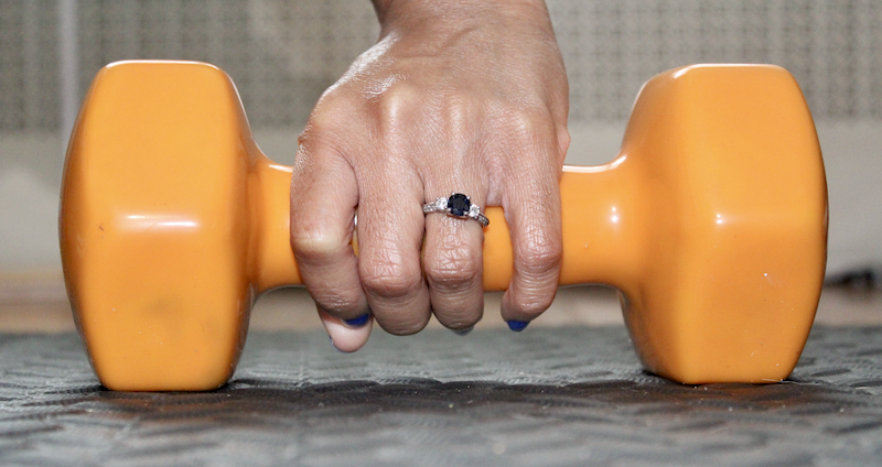 holding dumbbell with engagement ring on finger